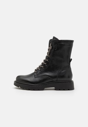Bottine noire en cuir avec un bout rond, surface texturée, accents de lacets métalliques et une semelle robuste. Dispose d'une sangle à l'arrière.