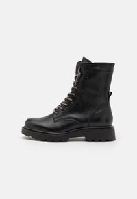 Bottine noire en cuir avec un bout rond, surface texturée, accents de lacets métalliques et une semelle robuste. Dispose d'une sangle à l'arrière.