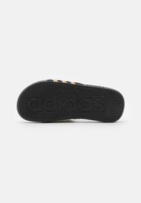 Svart sneakersåle med teksturert gummi, med gule tre striper og preget merkevarelogo. Flatt med rund tå og solid design.