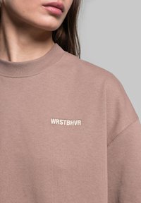 Brun sweatshirt med klassisk crew neck, prydet med broderet "WRSTBHV" branding på brystet, lavet af blødt bomuldsstof.