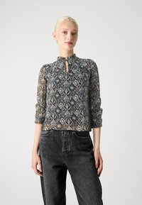 Blusa fluida e stampata nei toni del blu e marrone con scollatura a chiave e polsini arricciati. Abbinata a jeans in denim scuro.