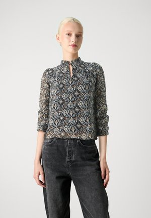 Lett, mønstret bluse i nyanser av blått og brunt med nøkkelhullhals og innsamlede mansjetter. Kombinert med mørke denimjeans.