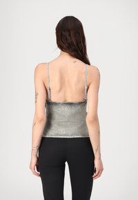 Ασημί μεταλλική κοντή τοπ με λεπτούς ρυθμιζόμενους ιμάντες, λεία υφή και ευθεία κοπή στο κάτω μέρος, εμφανιζόμενο από πίσω.