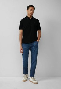 Schwarzes Polohemd mit kurzen Ärmeln und kontrastierendem Kragen, kombiniert mit blauen Jeans und beigen Sneakers. Einfaches Design, lässige Passform.