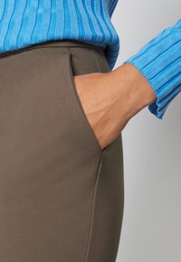 Blauer gerippter Pullover mit langen Ärmeln über einem braunen Stoff mit Seitentasche, der eine glatte Textur und eine figurbetonte Passform zeigt.