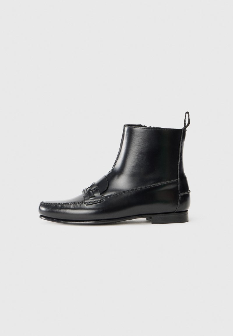Svart läderankelboot med rund tå, dekorativ rem och sydda detaljer. Slät textur och minimalistisk design med en liten klack.