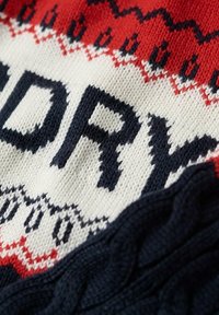 Sweter robiony na drutach w kolorach czerwonym, białym i granatowym. Teksturowany design z wyraźnym napisem i akcentem w splocie kablowym w kolorze granatowym.
