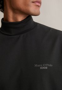 Μαύρο sweatshirt με ψηλό λαιμό, από μαλακό ύφασμα, με διακριτική επωνυμία "Marc O'Polo DENIM" σε γκρι χρώμα μπροστά, ντιζάιν με ψηλό γιακά.