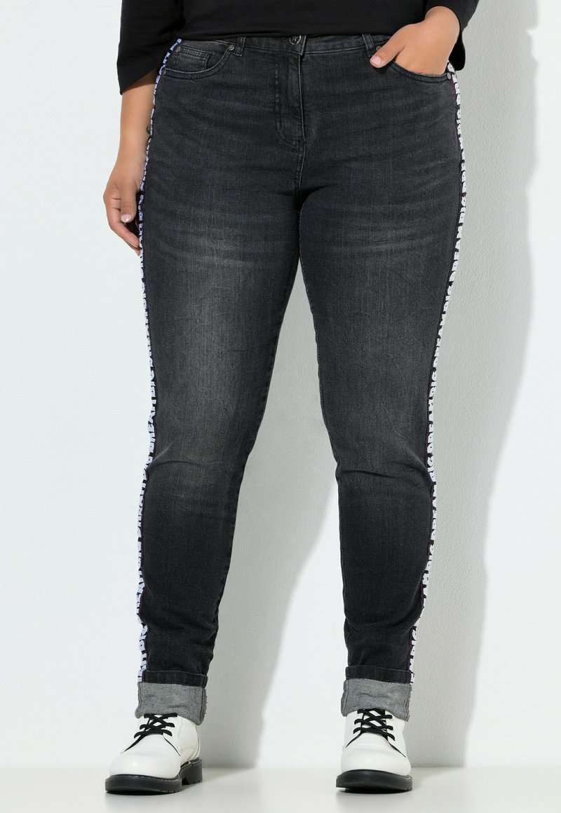 Jeans de denim gris oscuro con corte ajustado, que presentan una franja lateral con un diseño y dobladillos enrollados. El material es ligeramente texturizado y cuenta con bolsillos clásicos.