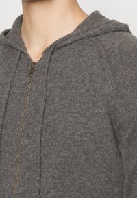 Grauer Reißverschluss-Hoodie aus weichem Stoff, ausgestattet mit einem Frontreißverschluss, einer Kapuze und gerippten Details entlang der Nähte.