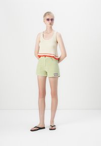 Strikket tank topp i kremfarge med røde og oransje striper; kordfløyelsgrønne shorts med lapp; svarte flip-flops. En enkel, uformell antrekk.