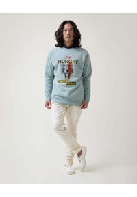 Sudadera azul claro con texto gráfico y un diseño de tigre, combinada con pantalones blancos y zapatillas blancas, con un corte relajado y escote redondo.