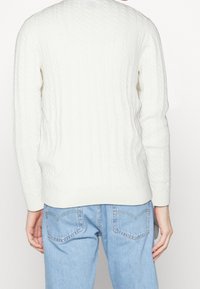 Kremowy sweter z grubym splotem, z długim rękawem i prążkowanymi mankietami, połączony z jasnoniebieskimi dżinsami. Miękka tekstura i luźny krój.