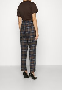 Tarkistettu housut, joissa on sininen ja ruskea kuvio, slim fit -leikkaus, korkea vyötärö ja sivutaskut. Yhdistetty mustiin korkokenkiin.