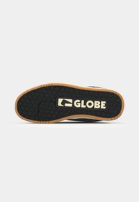 Black rubber shoe sole with intricate tread pattern, featuring a textured surface and a gum-colored edge. "GLOBE" logo in white.