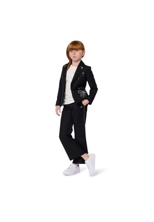 Zwarte dubbelgebreide blazer met versieringen, gecombineerd met zwarte broek en witte sneakers, met een wit t-shirt met ronde hals.