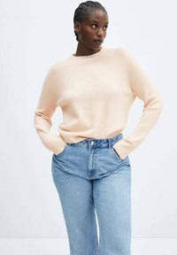 Lichtroze sweater met een ronde hals, lange mouwen en geribbelde manchetten, gecombineerd met hooggeknoopte lichtblauwe jeans. Zachte textuur, casual pasvorm.