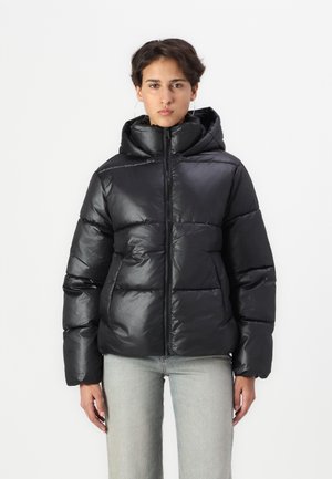 Veste matelassée noire avec une finition brillante, dotée d'une capuche, d'une fermeture éclair et d'un motif matelassé horizontal. Associée à un pantalon en denim clair.