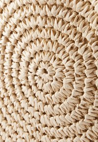 Rund matta av naturliga fibrer med ett tätt vävt spiralmönster. Ljust beige färg, med texturerade öglor och en mjuk, organisk känsla.