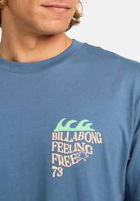 Sinine puuvillane t-särk, millel on graafika rohelise laine ja tekstiga "BILLABONG FEELING FREE 73" laimja ja hele roosa värviga. Ümmargune kaelus.