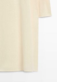 Off-white kortærmet skjorte med afslappet pasform hængende mod en hvid baggrund, der viser stoffets tekstur og syningsdetaljer.