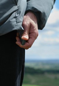Strângerea manuală a șnurului de ajustare de la manșa unei jachete albastre, cu un peisaj exterior neclar în fundal.