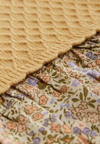 Pull en tricot moutarde avec une texture en diamant, associé à une jupe à motifs floraux dans des teintes de vert, rose et violet, avec des détails froncés.