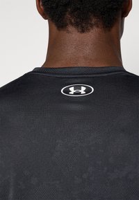 Zwart sportshirt met een gestructureerde stof, ronde halslijn en een wit logo-label op de achterkant.