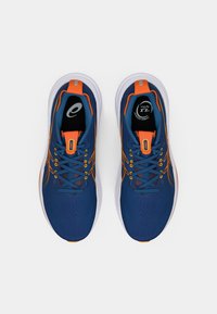 Scarpe da ginnastica blu con tomaia in rete, dettagli arancioni e suola bianca. Presentano un design con lacci e un collare imbottito per il comfort.