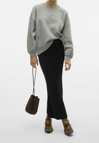 Sudadera gris de gran tamaño con un gráfico de una carita sonriente, combinada con una falda de punto negra, un bolso marrón oscuro y botas de tobillo marrón con estampado.