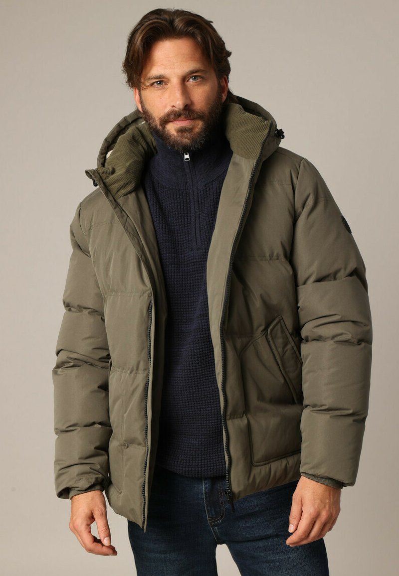 Doudoune vert olive avec une fermeture éclair à l'avant, une grande capuche et deux poches latérales. Pull texturé bleu marine en dessous. Coupe décontractée.