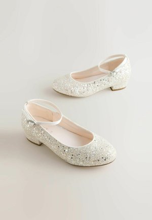 Glitzernde weiße Ballerinas mit rundem Zehenbereich, Knöchelriemen, niedrigem Absatz und einer glatten Innenausstattung. Die Schuhe sind mit silbernen Akzenten am Riemen versehen.