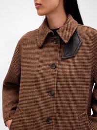 Palton cu model houndstooth maro, cu guler, accente din piele neagră pe umăr și nasturi negri. Include buzunare laterale.