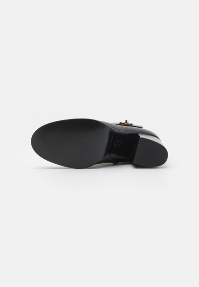 Stivale alla caviglia in pelle nera con punta arrotondata, texture liscia, suola piatta e dettagli in hardware color oro sui lati.