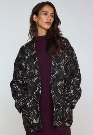 Zwarte oversized jas met een gedetailleerd geometrisch patroon in crème en bordeauxrood; zachte textuur en wijde mouwen.