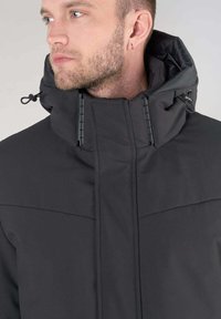 Zwarte hoodie met een hoge kraag, voorzien van een zachte textuur en verstelbare trekkoorden. Ritsen zichtbaar aan de voorkant.