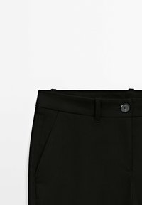 Pantalon noir à texture lisse, doté d'une fermeture à bouton, de passants pour ceinture et de poches latérales, présenté sur un fond blanc.