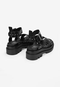 Sandalias de cuero negro con suelas de plataforma gruesa, con correas con tachuelas, hebilla ajustable y diseño de espalda abierta.