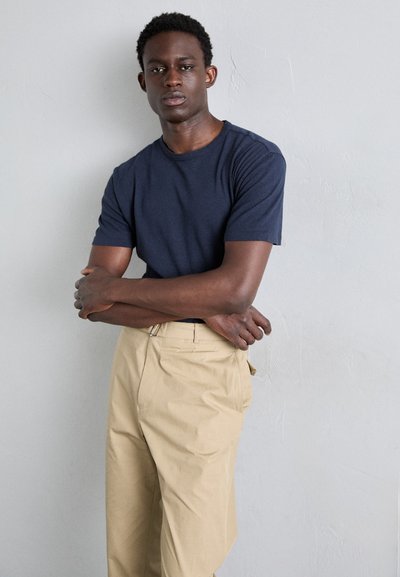 T-shirt en coton marine, à manches courtes, col ras du cou ; associé à un pantalon beige clair taille haute avec des jambes droites et des plis à l'avant.