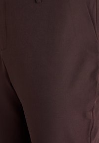 Rjave hlače iz gladkega materiala. Imajo krojen kroj, stranske žepe in čisto zaključek brez vidnih vzorcev ali okraskov.