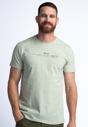 Helles grünes T-Shirt mit kurzen Ärmeln aus weichem Stoff. Mit einem Logo und Text, der horizontal in einer dunkleren Farbe gedruckt ist. Einfacher, lockerer Schnitt.
