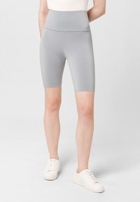Grijze hoge fietsbroekjes gemaakt van een gladde, rekbare stof, met een aansluitend ontwerp en een lengte tot halverwege de dij. Draag ze met witte sneakers.
