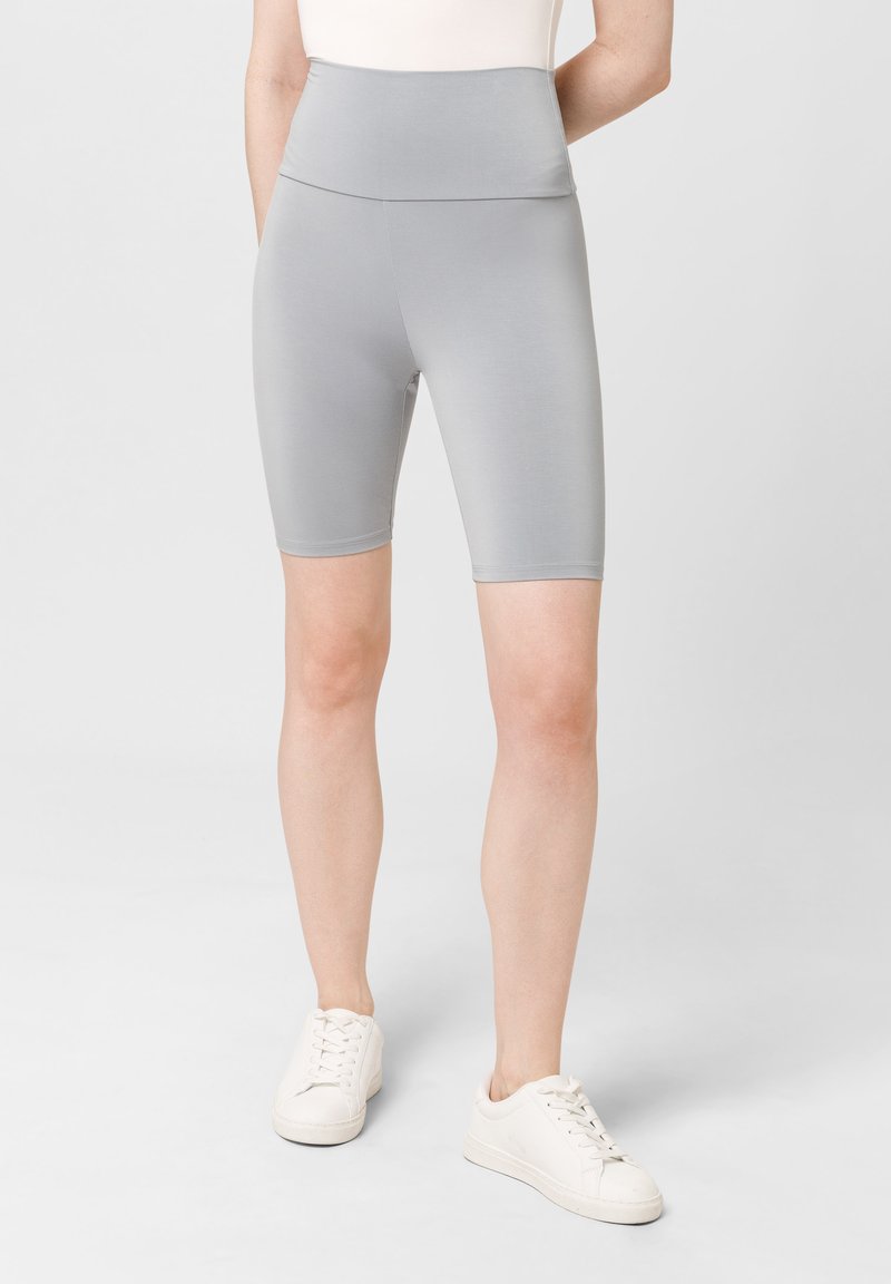 Culottes grises de ciclismo de tiro alto, hechas de un material suave y elástico, con un diseño ajustado y de longitud hasta medio muslo. Combinadas con zapatillas blancas.