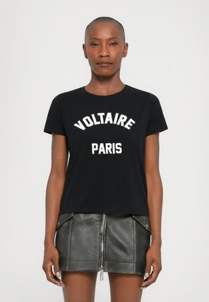 Sort bomulds T-shirt med hvid "VOLTAIRE PARIS" tryk. Den har rund halsudskæring og korte ærmer, som er parret med en grå læderskirt.
