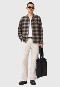 Brown and olive plaid shirt, white T-shirt, beige pants with textured accents, black tote bag, and sunglasses. Casual outfit presented.