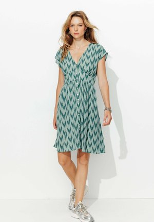 Robe verte à motifs avec un décolleté en V, des manches courtes et une fermeture à boutons. Le tissu texturé présente un motif en zigzag.