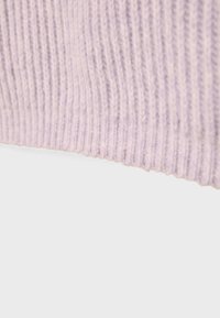 Ljust lila stickad tyg med ribbad textur. Bilden fokuserar på tygets kant, vilket visar en mjuk finish och jämn sömnad.