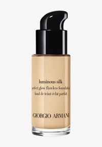 Luminous Silk foundationfles in helder glas, met een zwarte pompdeksel en zwarte tekst die het product en het merk labelt, beige vloeistof binnenin.