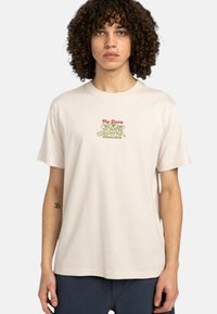 Krátky rukáv, béžové bavlnené tričko s grafickou potlačou s textom „The Doers“ v červenej a zelenej farbe, s voľným strihom a okrúhlym výstrihom.