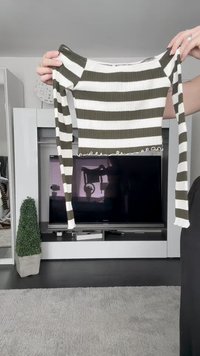 Olivno zelena in bela črtasta rebrasta kratka majica z dolgimi rokavi in obliko nabranega roba, ki jo drži oseba pred televizorjem.